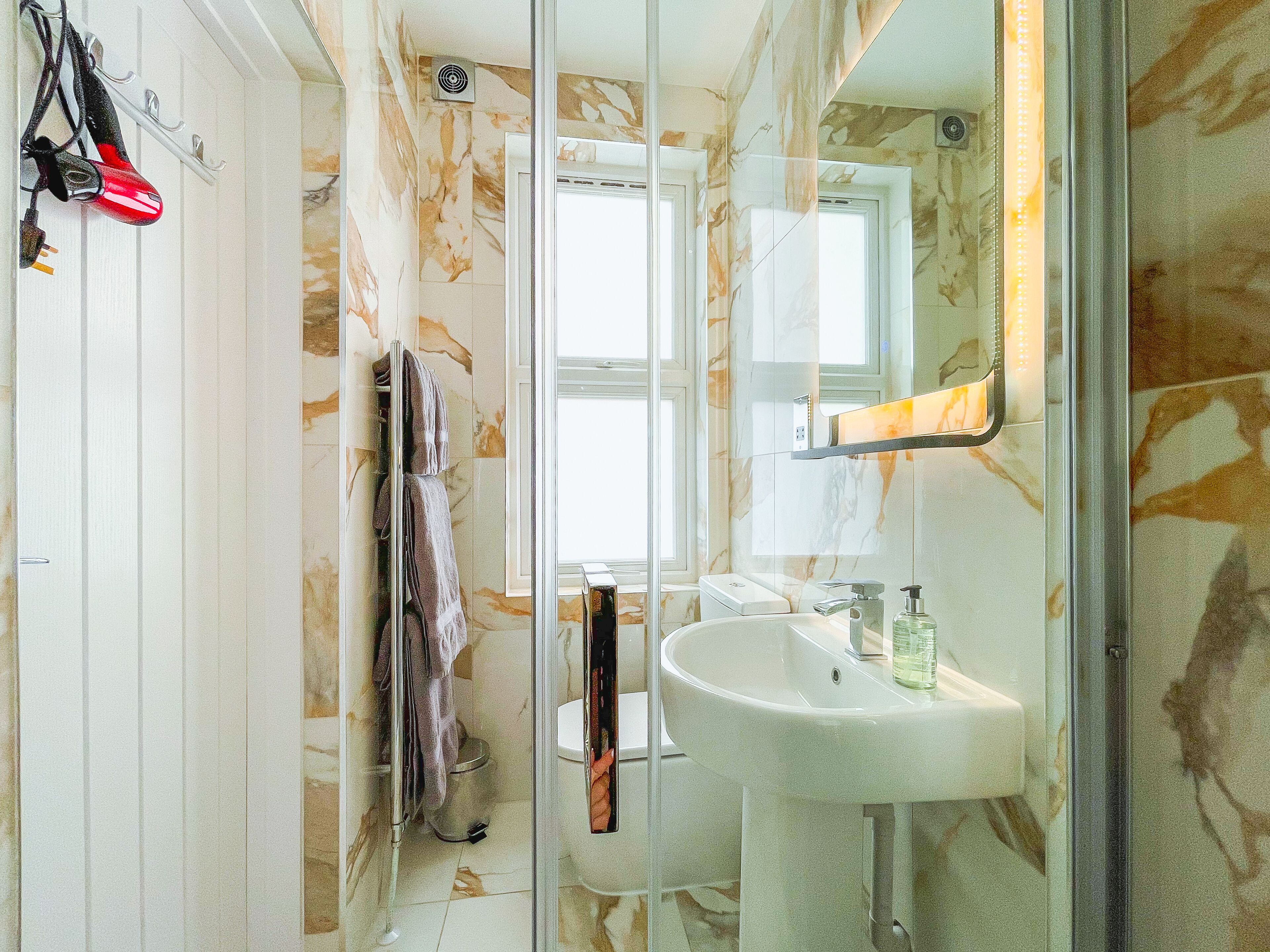 A bathroom with a glass shower enclosure, a white sink, and a towel rack.