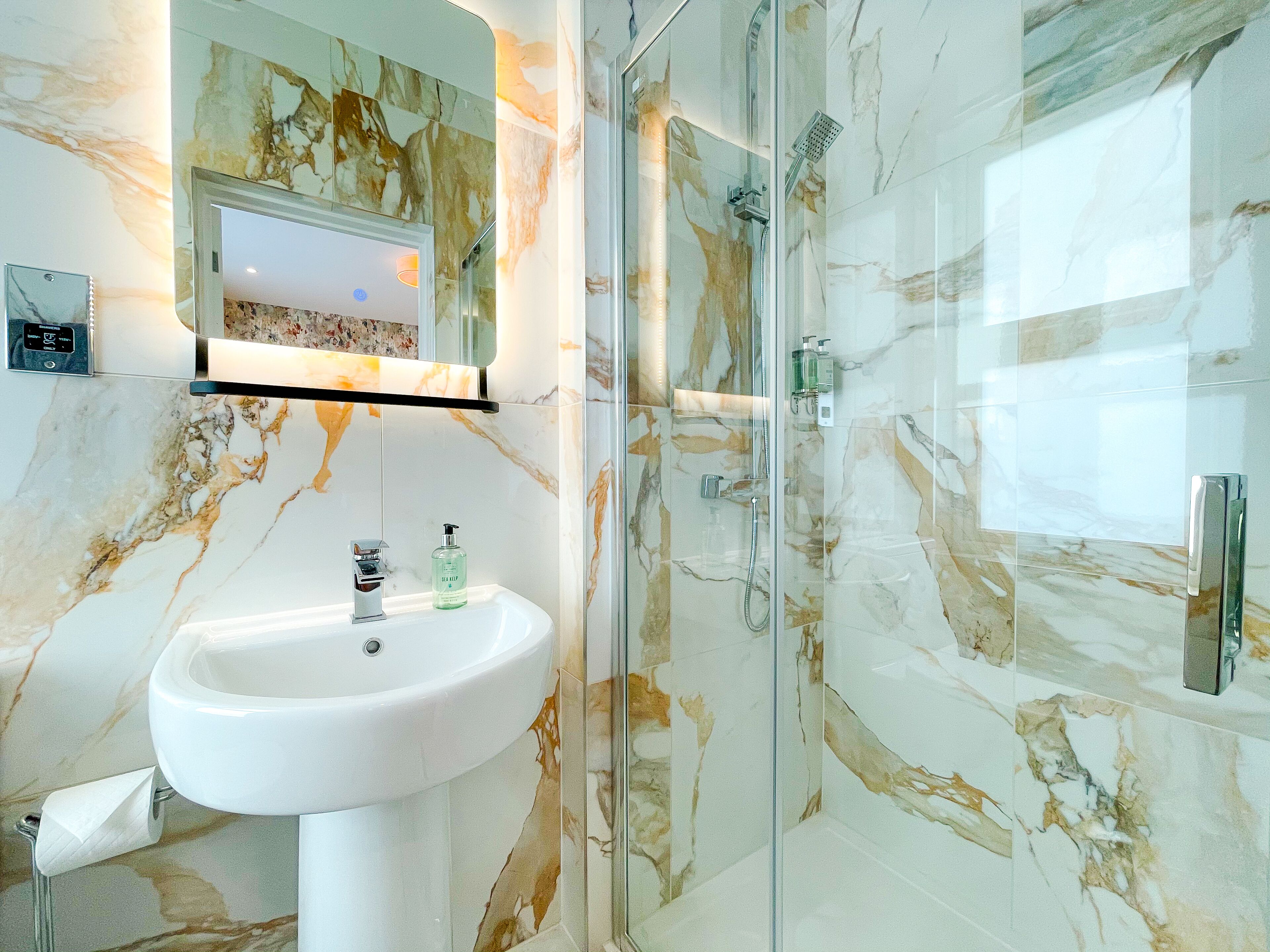 Een badkamer met een marmeren wastafel, een douchecabine van glas en een spiegel boven de wastafel.