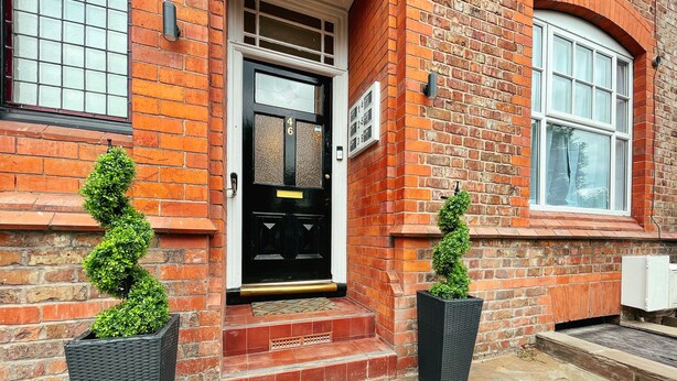 A brick building with a black door, numbered 46, and two potted topiary plants. - Ashfield Boutique Stays (Altrincham)