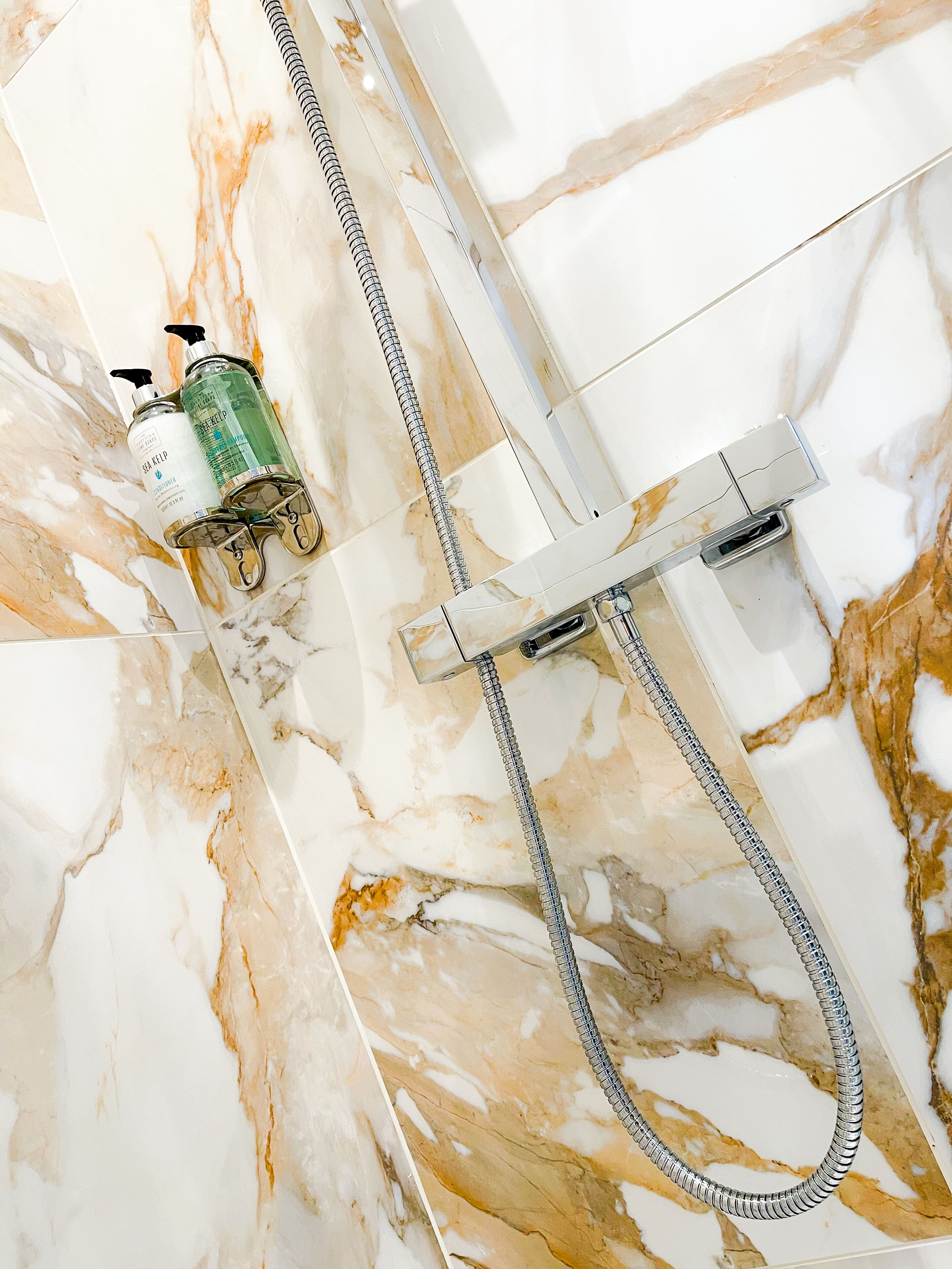 Ein Badezimmer mit Marmorboden, einer Dusche inklusive Handbrause sowie zwei Flaschen Shampoo und Conditioner.