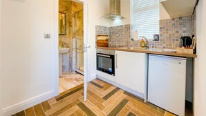 A compact kitchen with a tiled backsplash, a built-in oven, and a dishwasher. - Ashfield Boutique Stays (Altrincham)