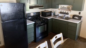 Una cocina compacta con armarios verdes, un refrigerador negro, una estufa, un microondas y un lavamanos.