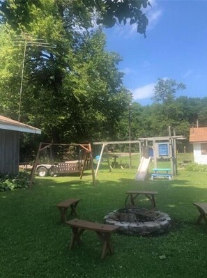 Relax in a serene outdoor space with a lawn, swing set, fire pit, picnic tables, and a playground.