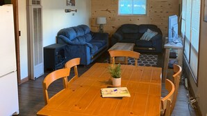 Una sala de estar acogedora con techo de madera, dos sofás, una mesa de comedor con sillas y un ventilador de techo.