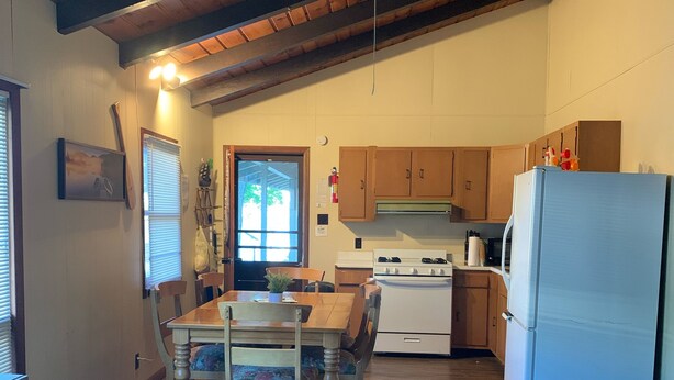 Una cocina acogedora con armarios de madera, una mesa de comedor con sillas y un refrigerador.