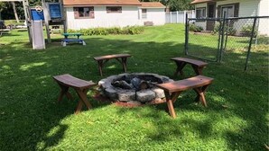Un patio trasero con una chimenea, mesas de picnic y un parque infantil.