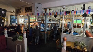 En bardel med flera olika sittplatser, inklusive barstolar och bord, samt ett stort urval av flaskor och dekorativa föremål på hyllorna.