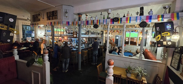 Una zona de bar con diversas opciones de asientos, incluyendo taburetes y mesas, y una variedad de botellas y adornos en las estanterías.