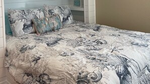 Een stapelbed met een onderste bed, een bed met een nautisch beddegoed en een wandplank met decoratieve items.