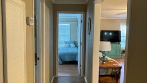 Een gang die leidt naar een slaapkamer met een bed, een nachtkastje en een lamp.