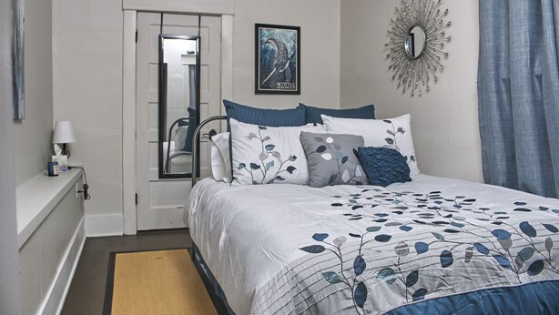 A bedroom with a bed, a door, a mirror, a wall clock, and a framed picture.