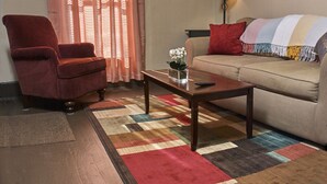 A living room with a red armchair, a beige sofa, a wooden coffee table, and a colorful rug.