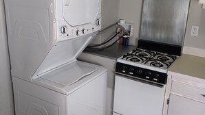 A compact kitchen with a white washer and dryer, a gas stove, and a stainless steel range hood.