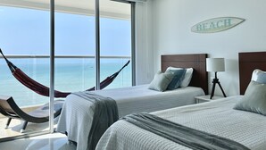 Habitación de hotel con dos camas, una hamaca, vista al océano y un letrero en la pared que dice 'BEACH'.