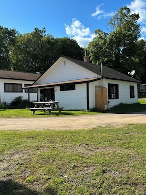 A white building with a sloped roof, a wooden door, and a picnic table in front. - Relaxing Cabin Getaway with Lake Front View!  (Garrison)