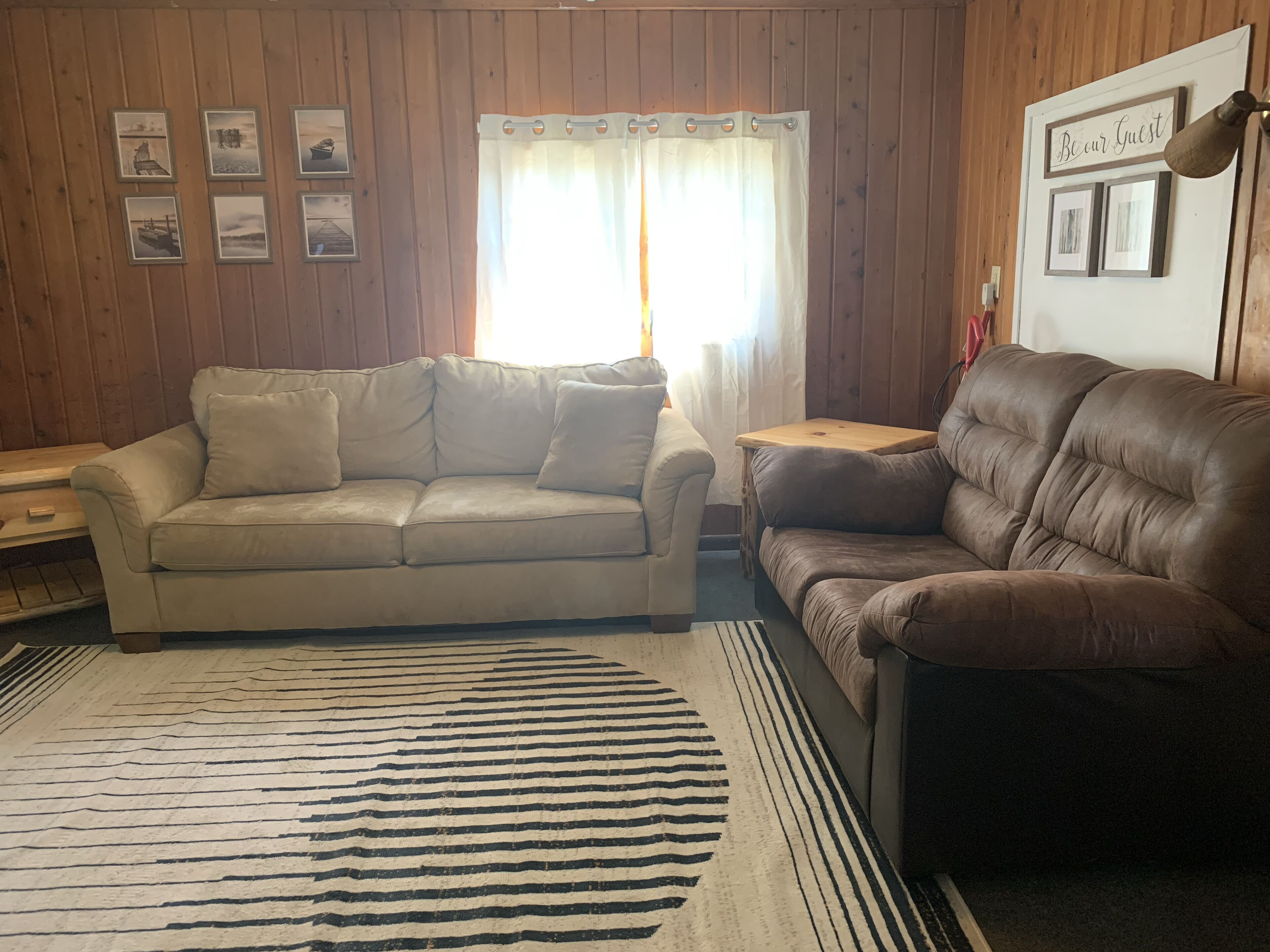 A living room with a beige sofa, a brown leather sofa, a wooden coffee table, and a striped rug.