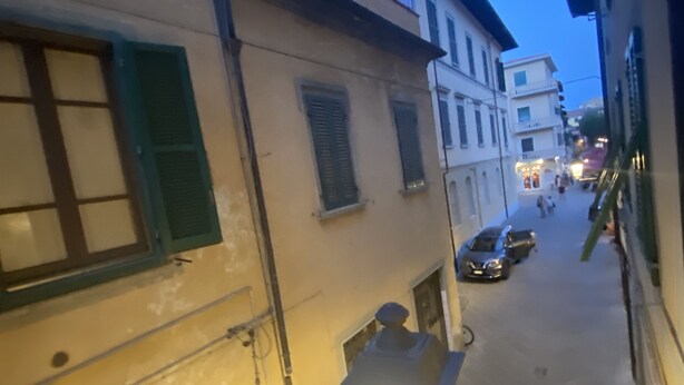 A narrow street with buildings on either side, featuring a mix of architectural styles and a small, illuminated street lamp. - Artemisia Pisa (Pisa)