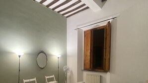 A bedroom with a bed, two chairs, a standing fan, and a window with a wooden shutter. - Artemisia Pisa (Pisa)