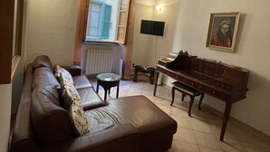 A living room with a brown leather sofa, a wooden piano, and a television on the wall. - Artemisia Pisa (Pisa)