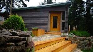 Een modern huis met een houten voordeur, stenen trappen en een tuin met rotsen en planten.