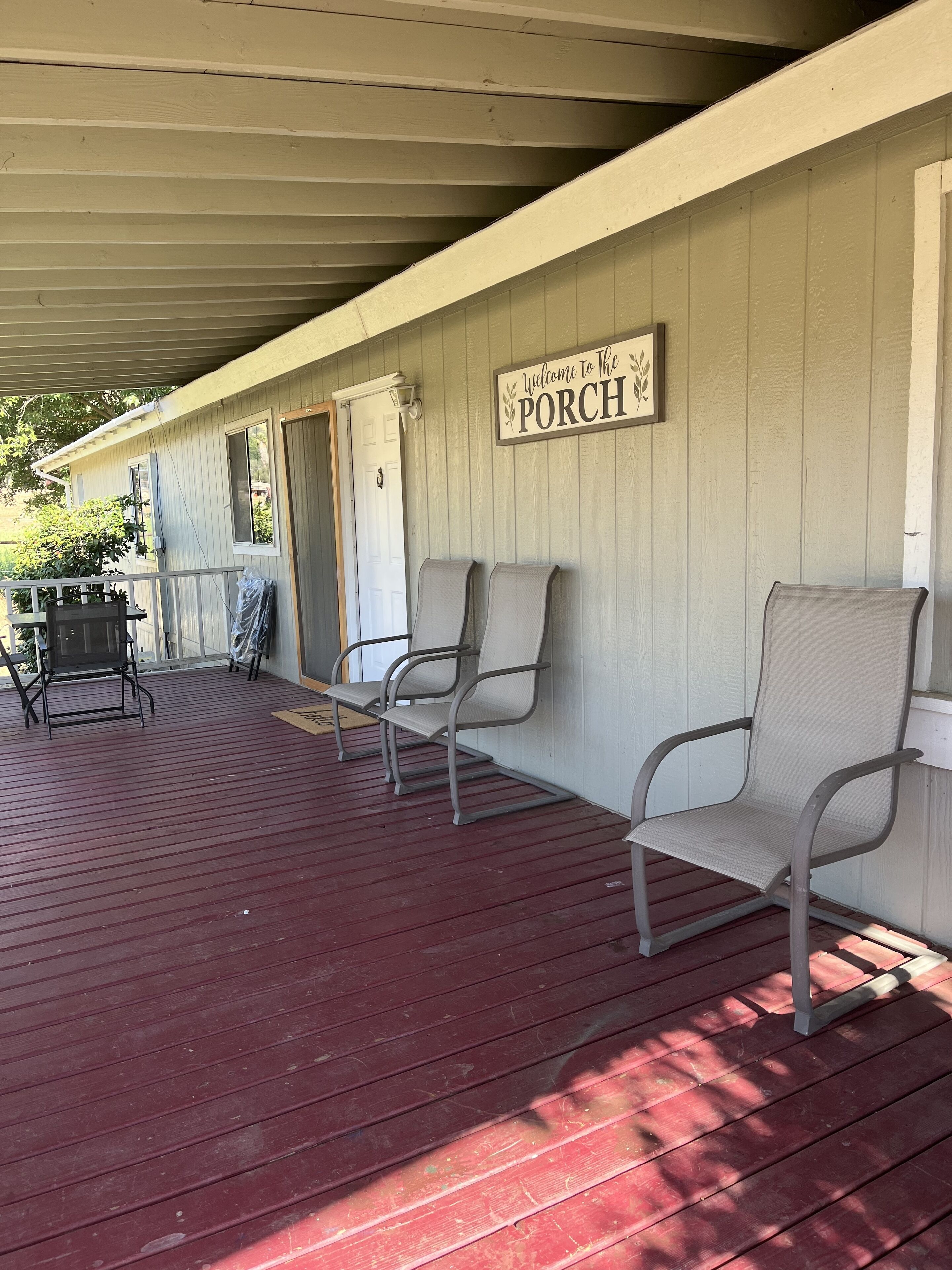 A covered porch with a red floor, two metal chairs, and a 'Welcome to The Porch' sign.