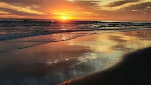 Une plage où le soleil se couche sur l’océan, créant une surface d’eau calme et propice à la contemplation.