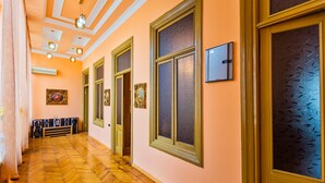 A hallway with wooden flooring, large windows with frosted glass, and framed artwork on the walls.