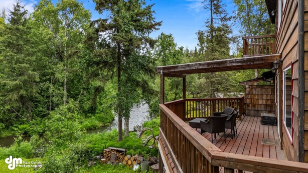Eine Holzterrasse mit Gartenmöbeln, mit Blick auf einen Wald und ein Gewässer.