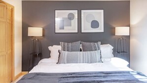 Ein modernes Schlafzimmer mit einem Bett, zwei Nachttischlampen und zwei gerahmten abstrakten Kunstwerken an der Wand.