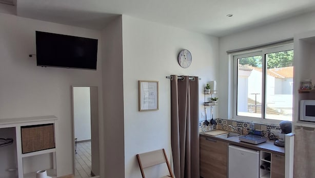 A modern kitchen with a dining area, a flat-screen TV, a clock, and a window with a view of the outside.