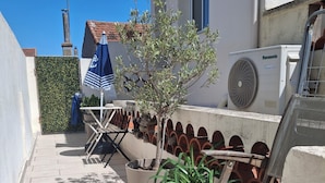 A rooftop terrace with a seating area, a small tree, and an air conditioning unit.