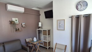 A modern living room with a sofa, a small table, a chair, a TV, and a clock on the wall.
