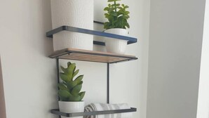 A kitchen with a tiled backsplash, a hanging pot rack with plants, a wooden shelf, and a basket with a bottle.