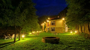 A two-story house with a well-lit lawn, a fire pit, and outdoor seating. - Pine Park Edge Resort Khanian (Balakot)