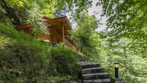 A wooden cabin with a red roof, surrounded by lush greenery and stone steps leading up to it. - Pine Park Edge Resort Khanian (Balakot)