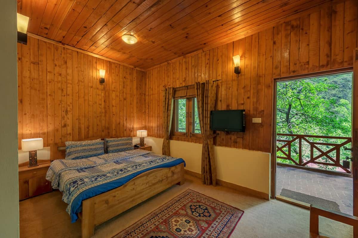 Ein Schlafzimmer mit Holzwandverkleidung, einem Bett, zwei Nachttischlampen, einem Fernseher und Blick ins Freie.