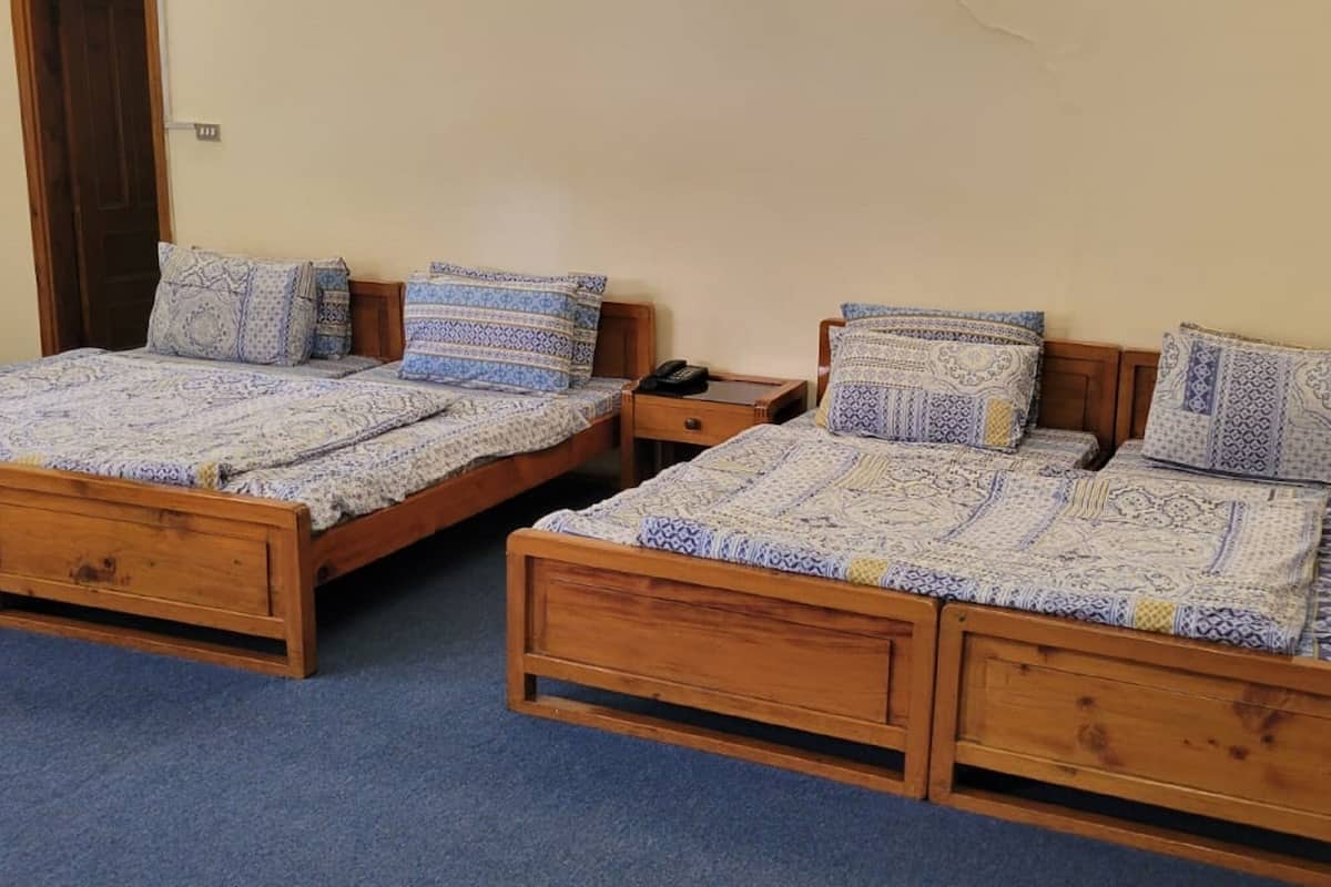 Zwei hölzerne Betten mit gemusterten Betttextilien, ein Nachttisch aus Holz und ein blauer Teppich.