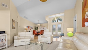 A spacious living room with a white leather sofa, a glass coffee table, and a dining area with orange chairs. - A twist of tropical passion - SW Cape (south facing) with fully Inclusive rates (Cape Coral)