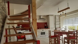 Une cuisine moderne avec des meubles blancs, un mur d’accent rouge et un coin repas comprenant des chaises et une table en bois.