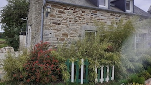 Une maison en pierre avec un toit en pente, une petite fenêtre et une clôture blanche en bois.