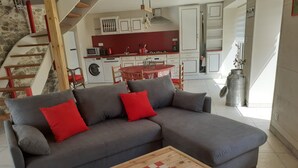 Un salon avec un canapé d’angle gris, des coussins rouges et une table basse en bois à motifs à carreaux.