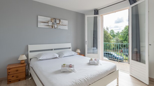 A modern bedroom with a large bed, a bedside table, a nightstand, a wall-mounted artwork, and a balcony with a view of the outside. - La Saline - Wifi - Parking - Jardin (Villeneuve-en-Retz)