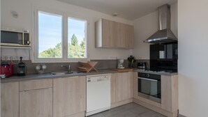 A modern kitchen with light wood cabinets, a stainless steel range hood, a dishwasher, and a window providing natural light. - La Saline - Wifi - Parking - Jardin (Villeneuve-en-Retz)