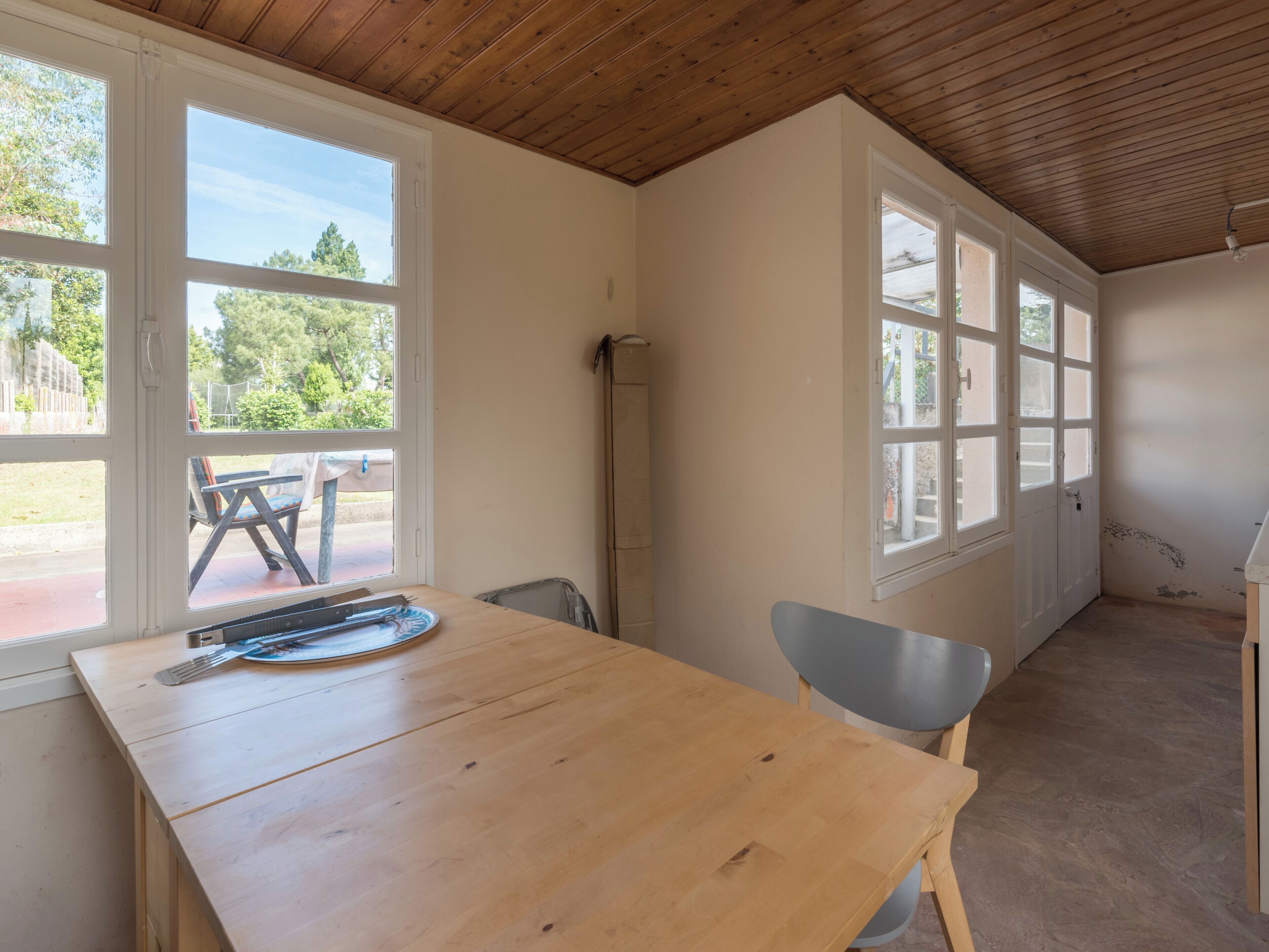 Une pièce avec une table et des chaises en bois, de grandes fenêtres et une vue sur l’extérieur.