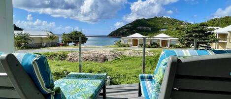 Um terraço com duas espreguiçadeiras, uma mesa pequena e vista para o mar e colinas ao fundo.