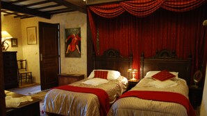 Une chambre à coucher de style traditionnel, avec deux lits, une tête de lit en bois, un rideau rouge et une lampe sur une table de chevet.
