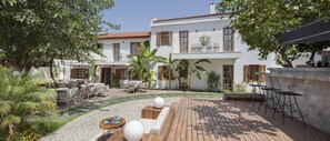 A two-story white building with a red-tiled roof, outdoor seating area with tables and chairs, and a wooden deck. - Mellow Blue Hotel (Seferihisar)