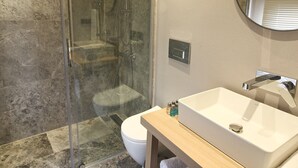 Un baño moderno con ducha de vidrio, lavamanos blanco y tocador de madera.