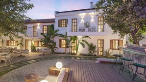 Un patio con mobiliario exterior, una piscina y un edificio con varias ventanas y balcones.