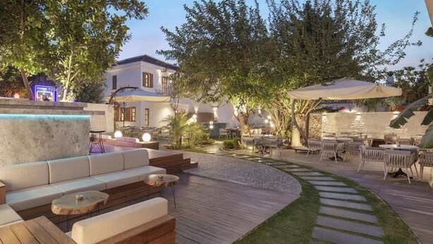 Un espacio al aire libre con una terraza de madera curvada, asientos acolchados y una pequeña fuente.